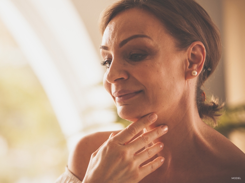 mature woman touching her neck meant to represent a person considering neck lift surgery